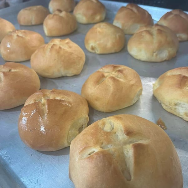 Freshly baked golden-brown dinner rolls with cross-shaped cuts on a baking sheet.